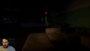 Ein sehr dunkler Raum in dem eine Puppe in der Ferne zu sehen ist. Im Vordergrund des Bildes ist eine Art Couch zu sehen.